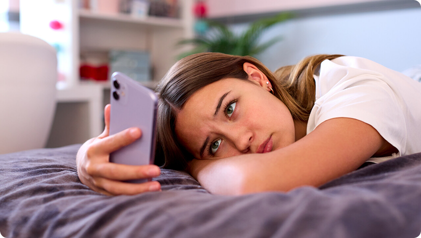 Teenager alone in her bedroom looking at her cell phone with sad and worried traits.